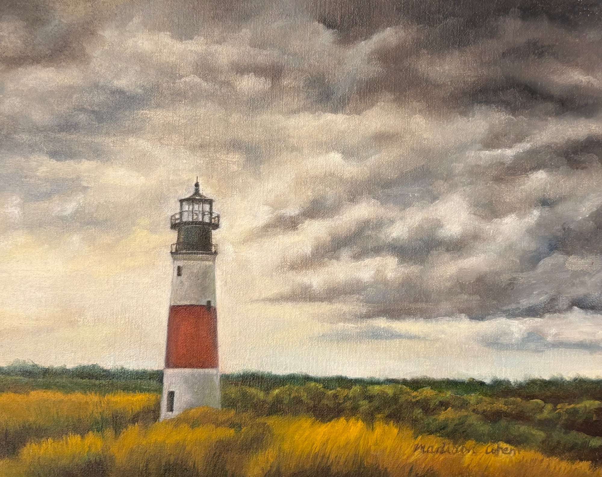 A red-and-white banded lighthouse standing above golden marsh grass beneath a heavy bank of dark storm cloud, with a band of pale light along the horizon.
